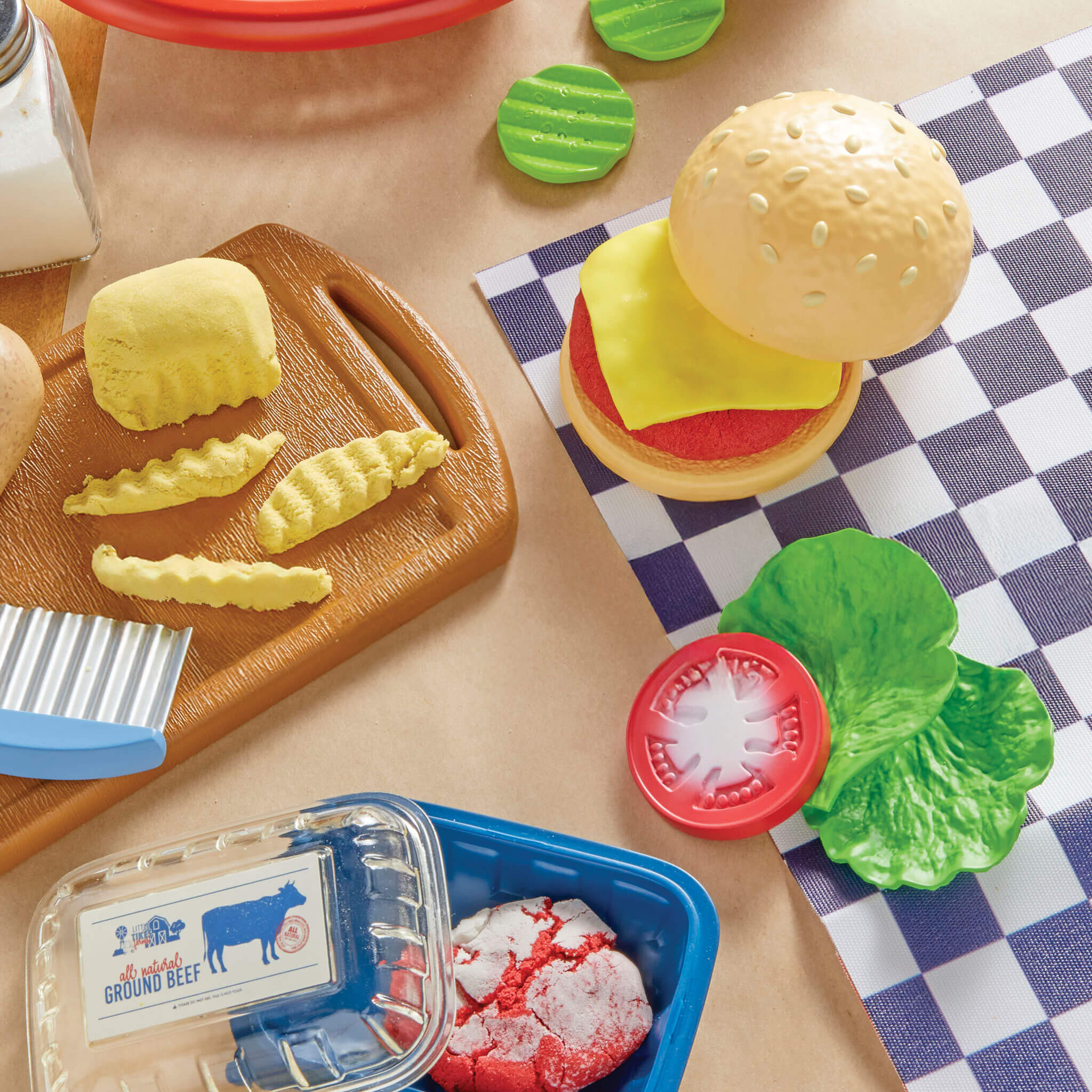 Play food set with hamburger, fries, and ground beef on a checkered tablecloth.