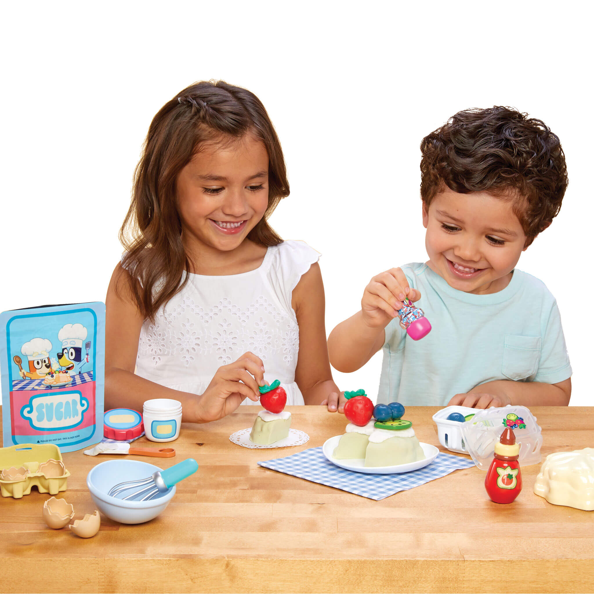 Two children playing with Pavlova and utensils on a wooden table.