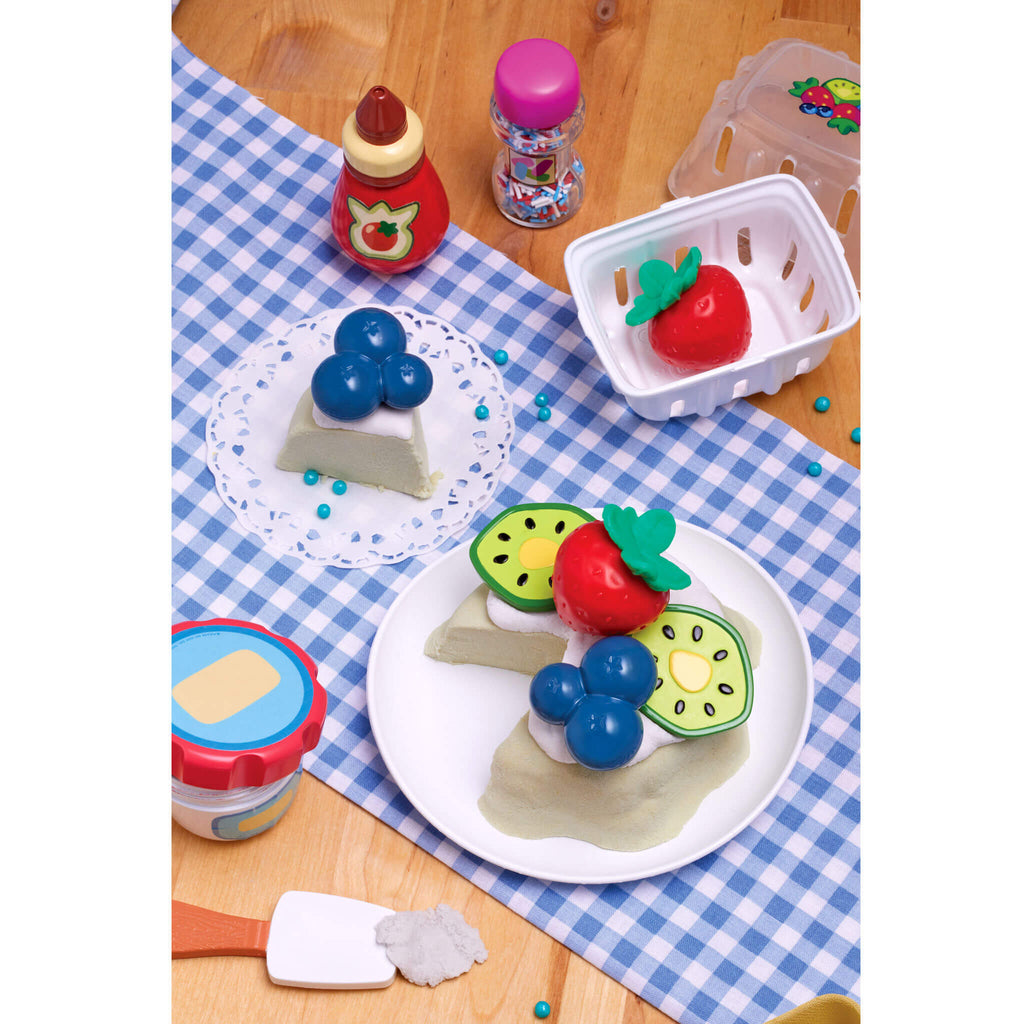 food set on a checkered tablecloth with various toy fruits and containers.